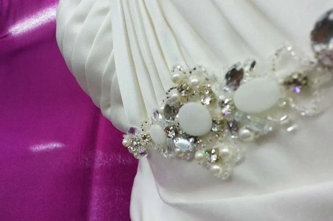 Detailaufnahme eines Brautkleids mit Perlen- und Strassapplikation auf gerafftem Satin