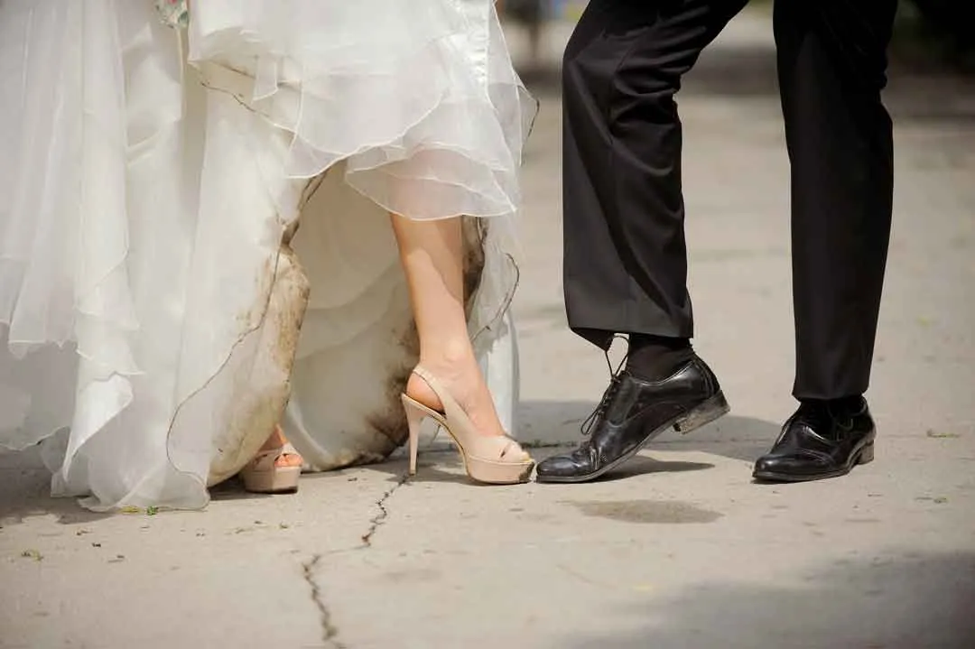 Verschmutzter Saum eines weißen Brautkleids neben den Schuhen des Bräutigams nach der Hochzeit