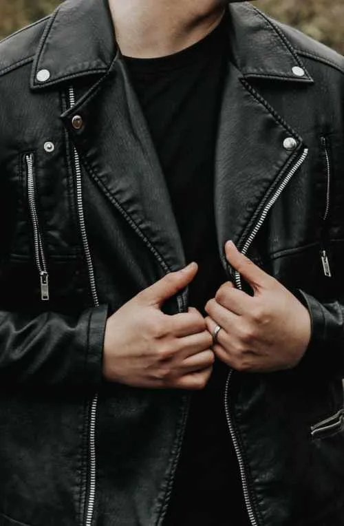 Schwarze Lederjacke mit Reißverschlüssen und Nieten, von einer Person geschlossen gehalten
